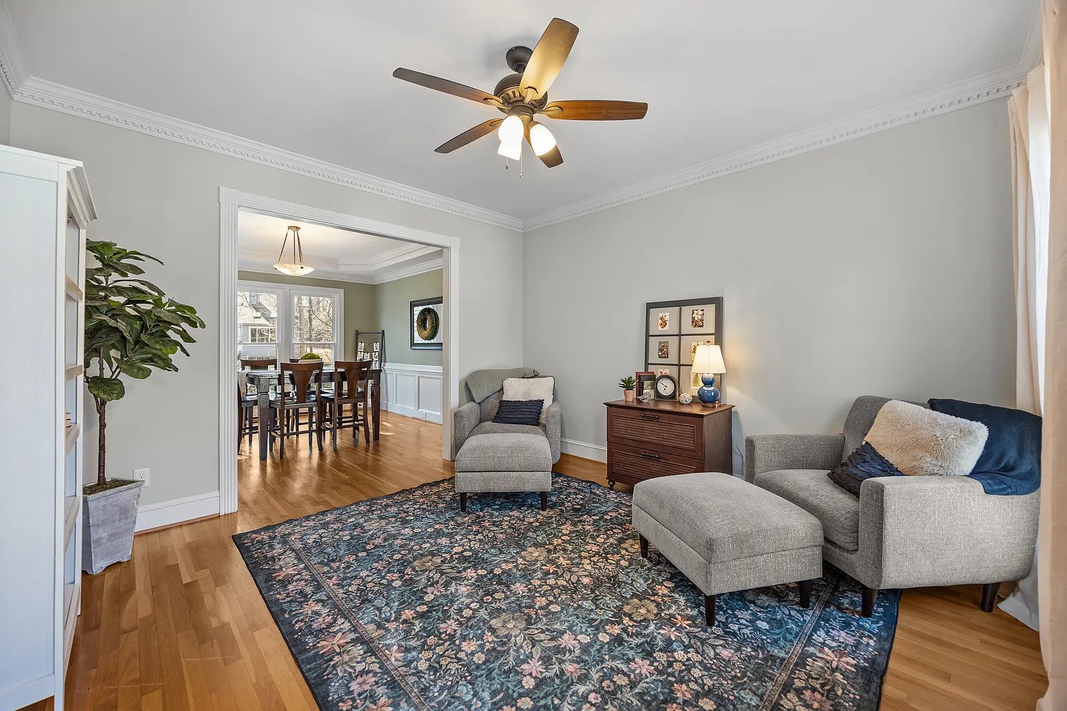 A staged sitting room with floral rug and gallery wall, viewed toward the dining room