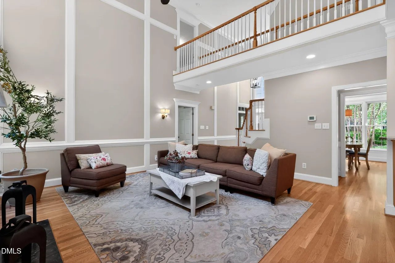 A two-story staged living room with neutral sofa and olive tree